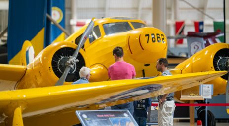 Groupe de personnes observant un avion d’époque jaune portant le numéro 7862 sur son nez, à l’intérieur d’un musée de l’aviation.