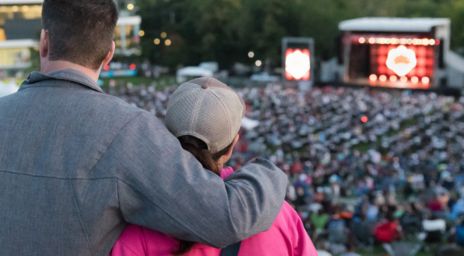 Un homme avec le bras autour d’une femme regardant la scène principale au loin