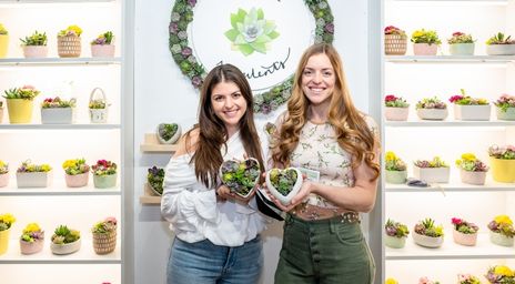 Two women holding succulent in a heart-shaped pot at One of a Kind Spring Show