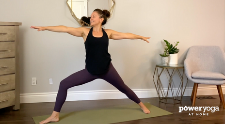 Une femme faisant une pose de yoga Warrior dans son salon
