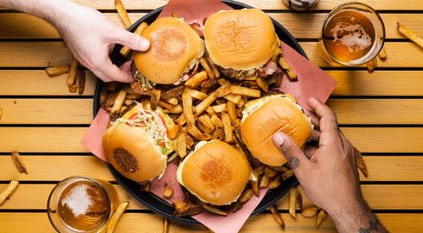 Des amis saisissant un burger de Mikey’s Smash Burgers sur une assiette avec des frites